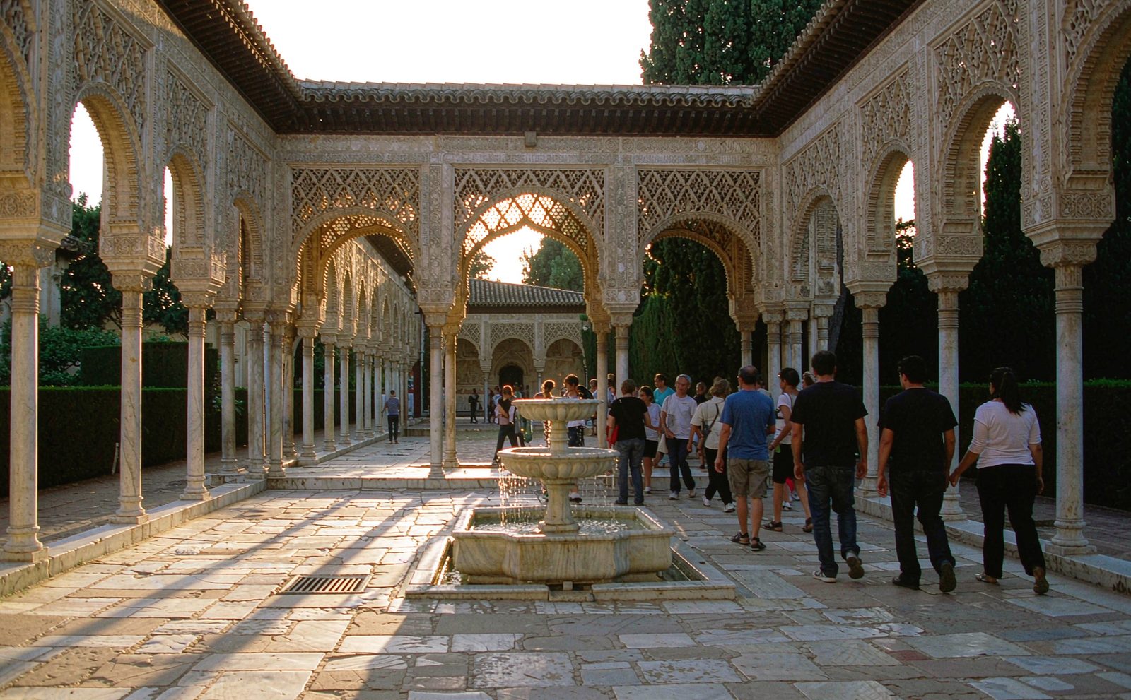 Visitors in a Nasrid palace courtyard in Granada, carved stucco arches and a still reflecting pool