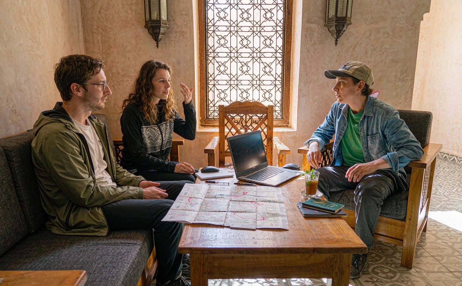Two travellers planning a trip over maps and a laptop in a bright cafe