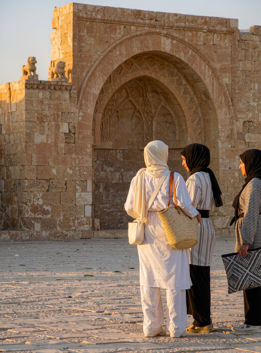 Muslim women travellers in hijab walking through a sunlit historic stone courtyard